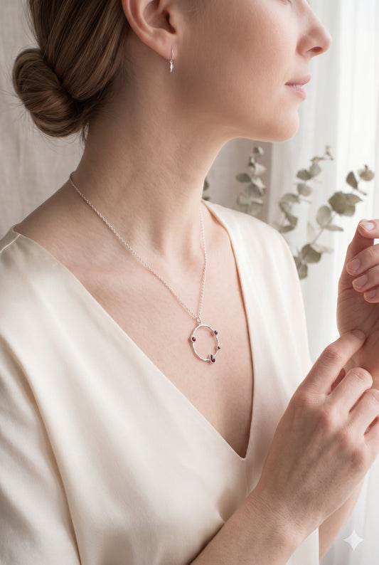 Model wearing a sterling silver hammered circle necklace with deep red garnet accents against a cream V-neck blouse.