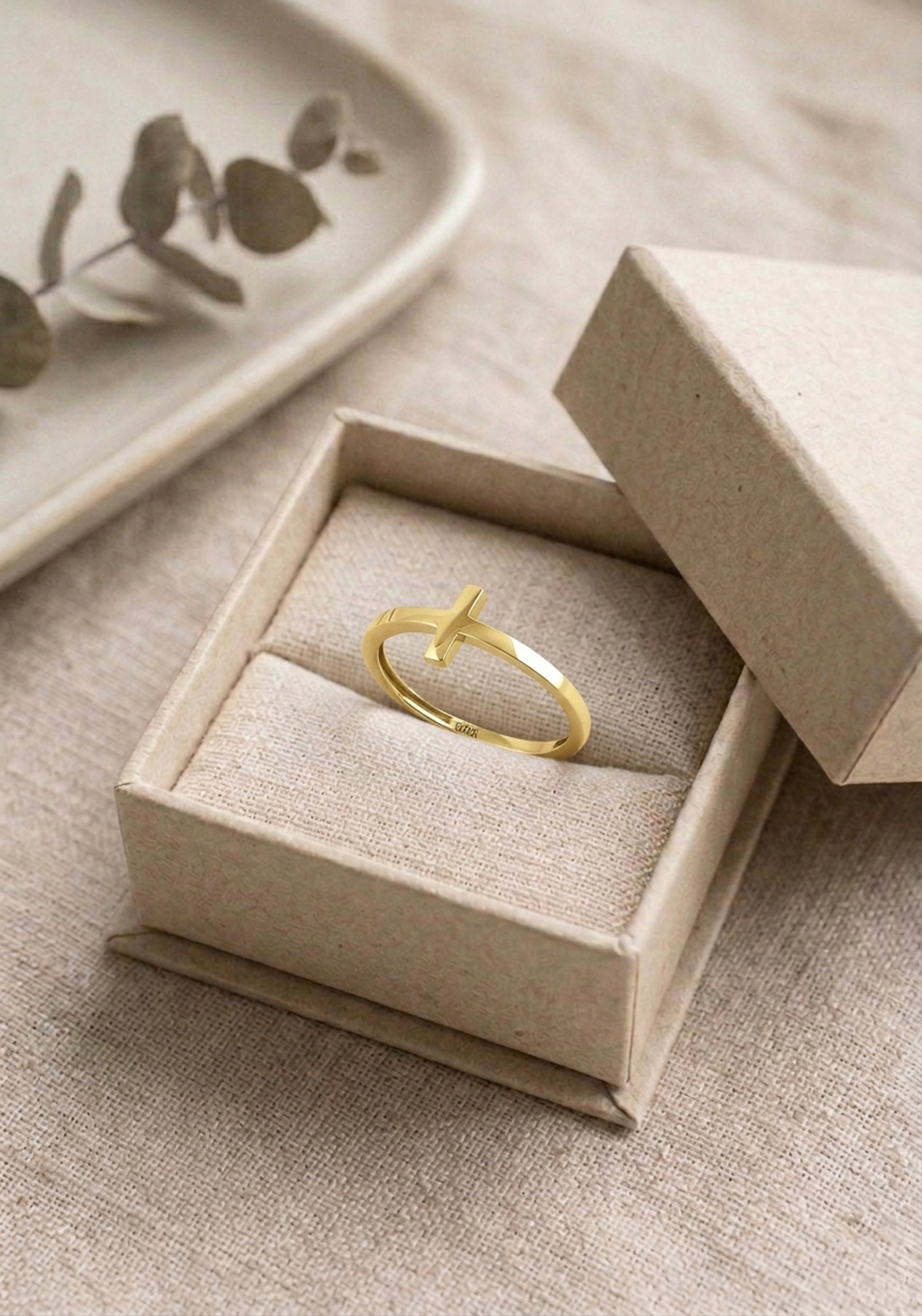 A dainty gold cross ring presented in linen jewelry gift box on a linen surface. The ring features a sideways cross design with a high-polish finish, shown as a meaningful gift idea for baptism, confirmation, or a religious bridesmaid gift.