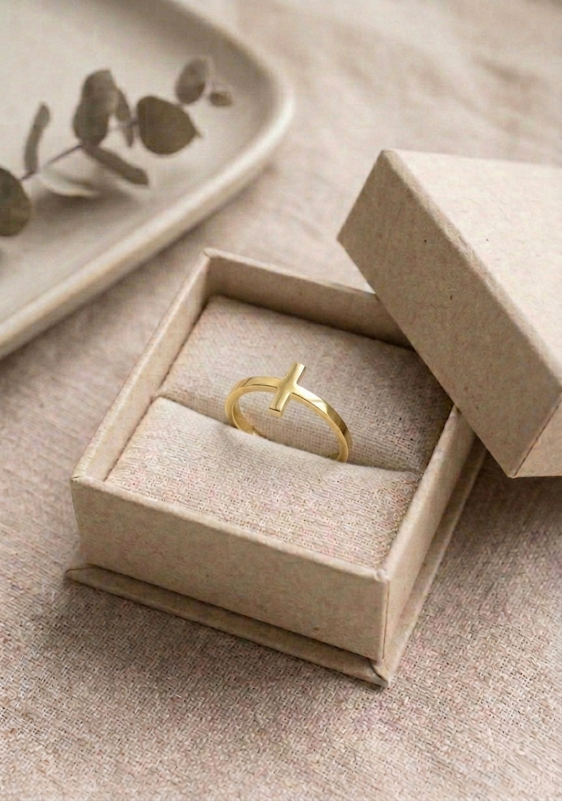 A dainty gold cross ring presented in linen jewelry gift box on a linen surface. The ring features a sideways cross design with a high-polish finish, shown as a meaningful gift idea for baptism, confirmation, or a religious bridesmaid gift.