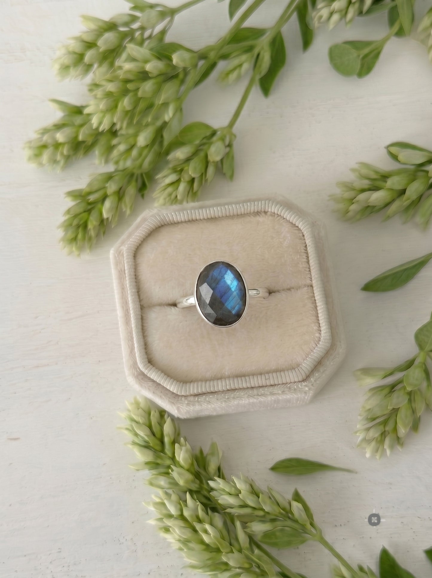 Oval labradorite ring with blue flash in a cream velvet engagement box on a white wood background. Handmade silver gemstone ring, ideal for unique promise rings or a dainty boho bridal gift.