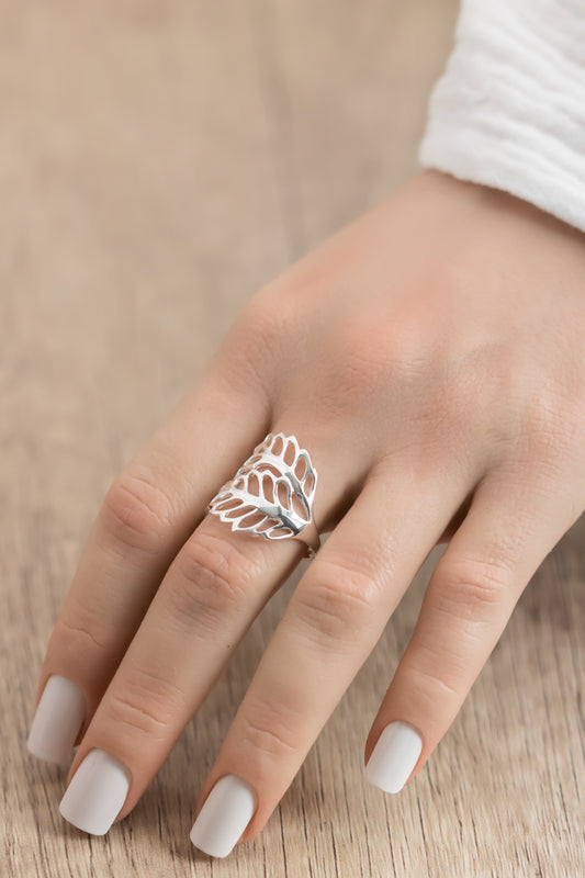 Silver leaf-shaped ring on a finger with a neutral background