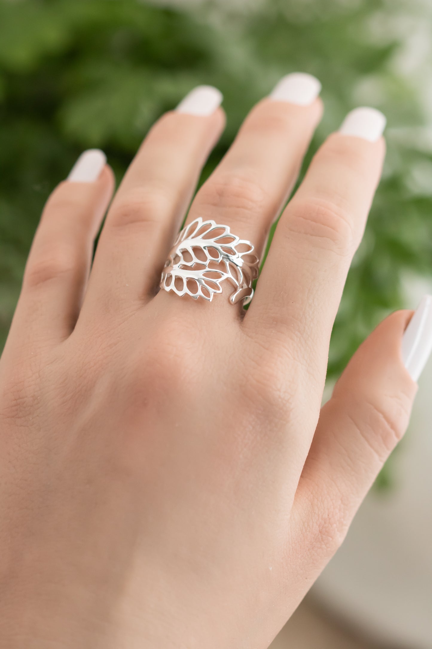 Silver leaf-shaped ring on a hand with a blurred green background