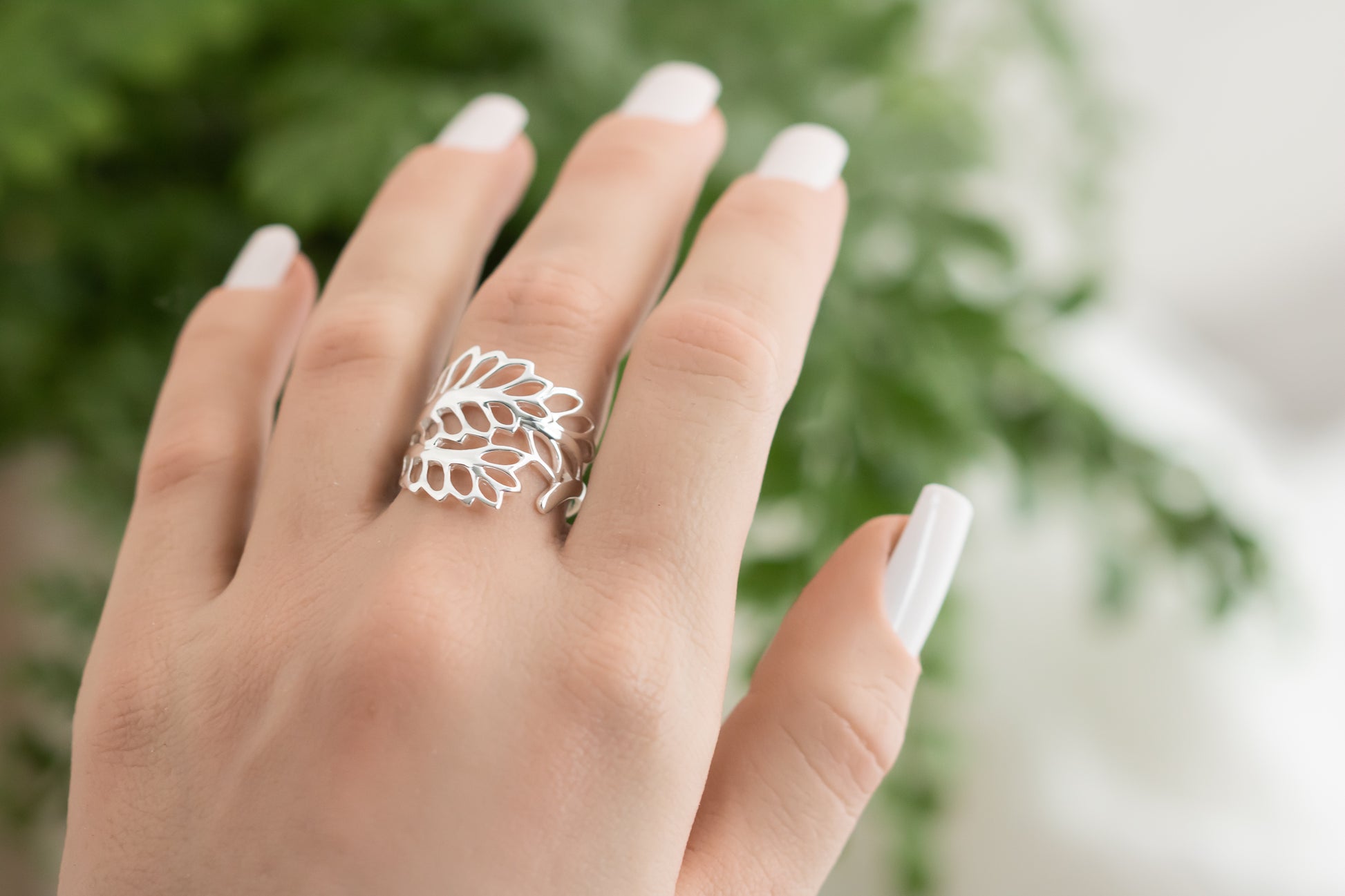 Hand wearing a silver leaf-shaped ring with a blurred green background