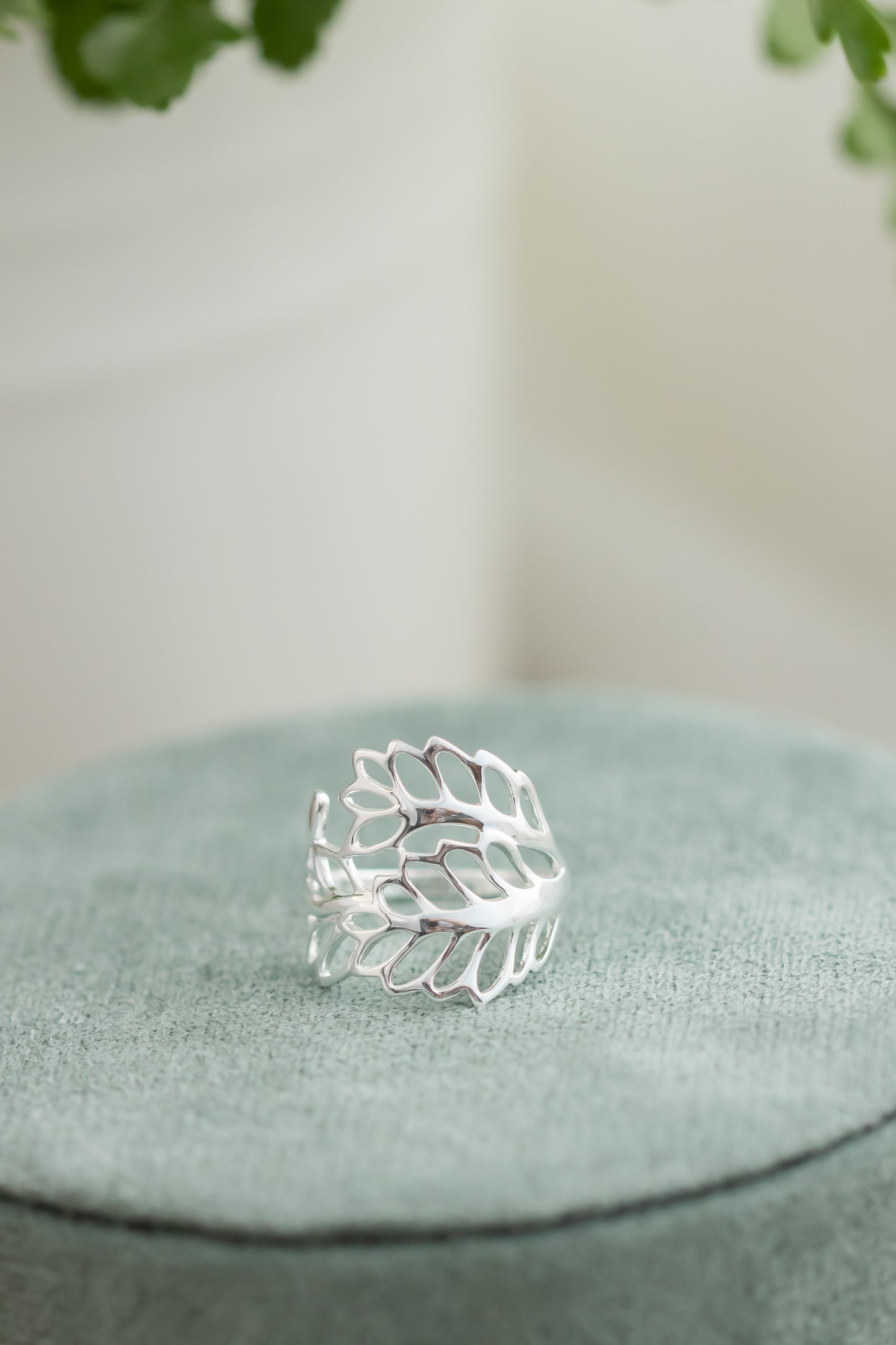 Silver leaf-shaped ring on a textured green surface with a blurred natural background