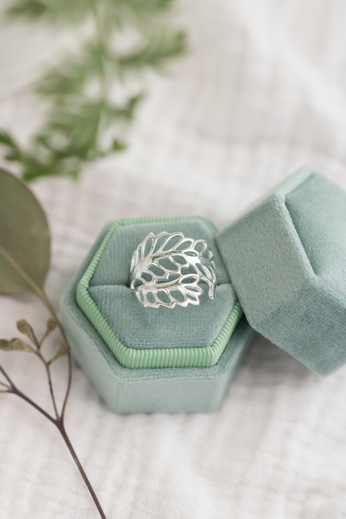 Silver ring in a green jewelry box on a light background