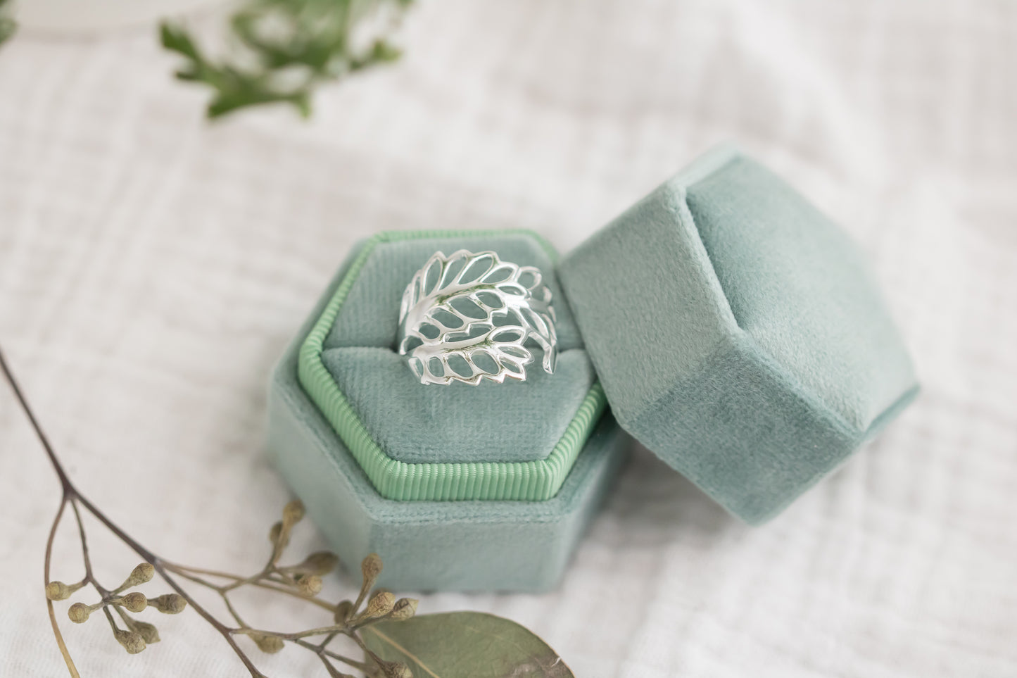 Silver ring in a hexagonal green velvet box on a light background