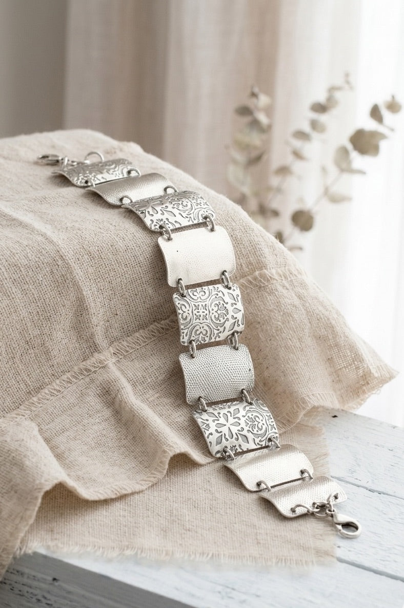 Close-up of sterling silver rectangle links showing oxidized and brushed texture detail. The bracelet features 7, 1.25 inch x 3/4 inch wide, curved segments, each adorned with detailed floral and geometric engravings. The segments are connected by small metal loops, and a lobster clasp.
