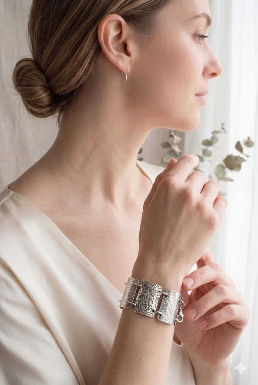 Woman wearing a silver bracelet with  intricate designs. Close-up of sterling silver rectangle links showing oxidized and brushed texture detail. The bracelet features 7, 1.25 inch x 3/4 inch wide, curved segments, each adorned with detailed floral and geometric engravings. The segments are connected by small metal loops, and a lobster clasp.

