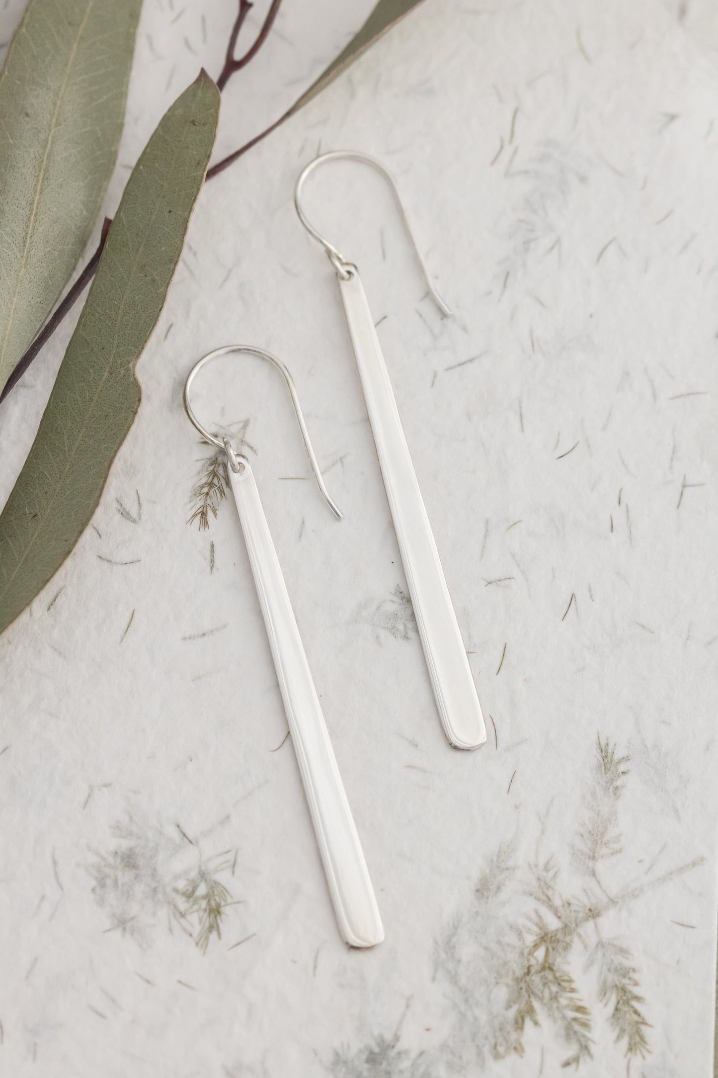 Silver earrings on a textured white surface with green leaves