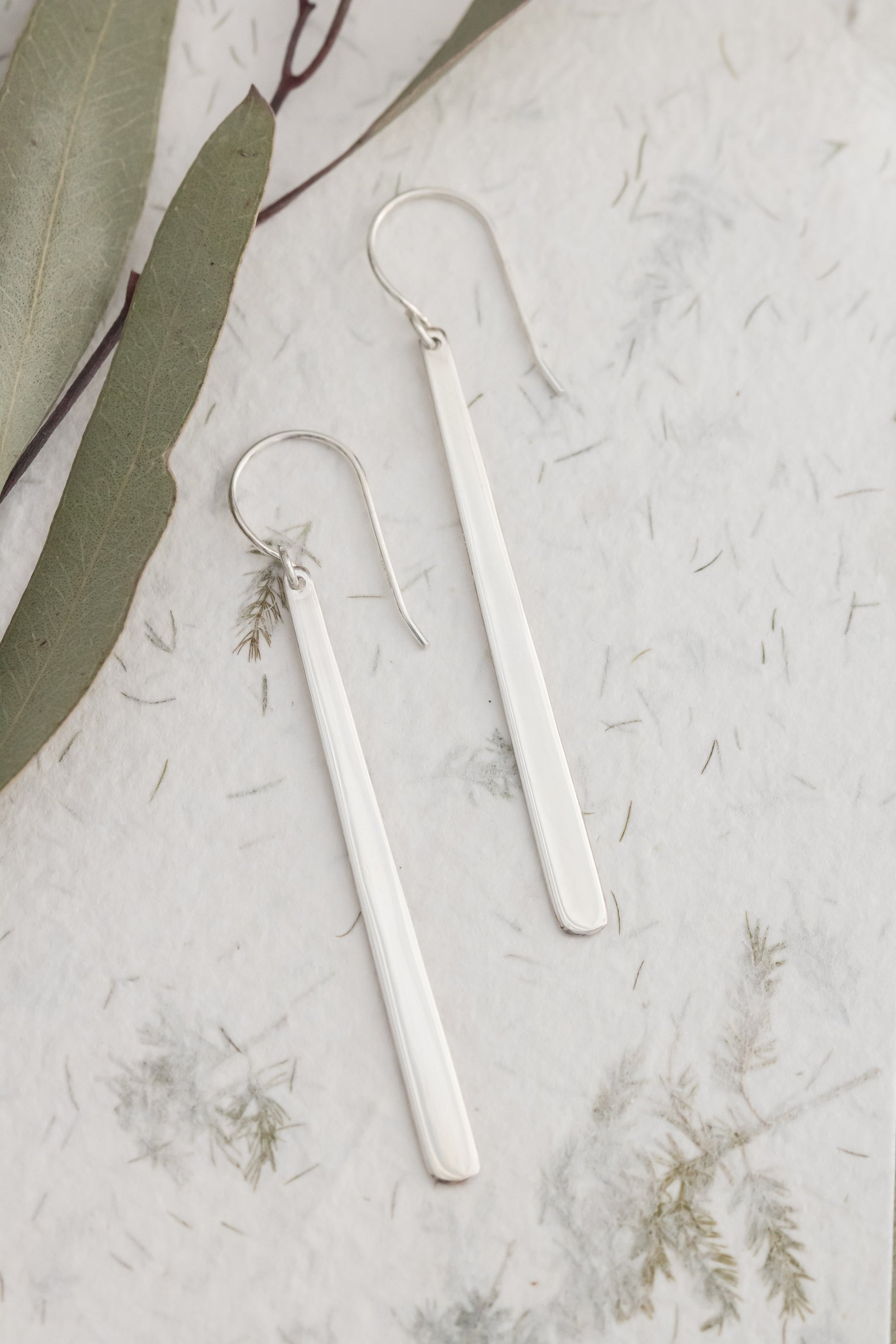 Silver earrings on a textured white surface with green leaves
