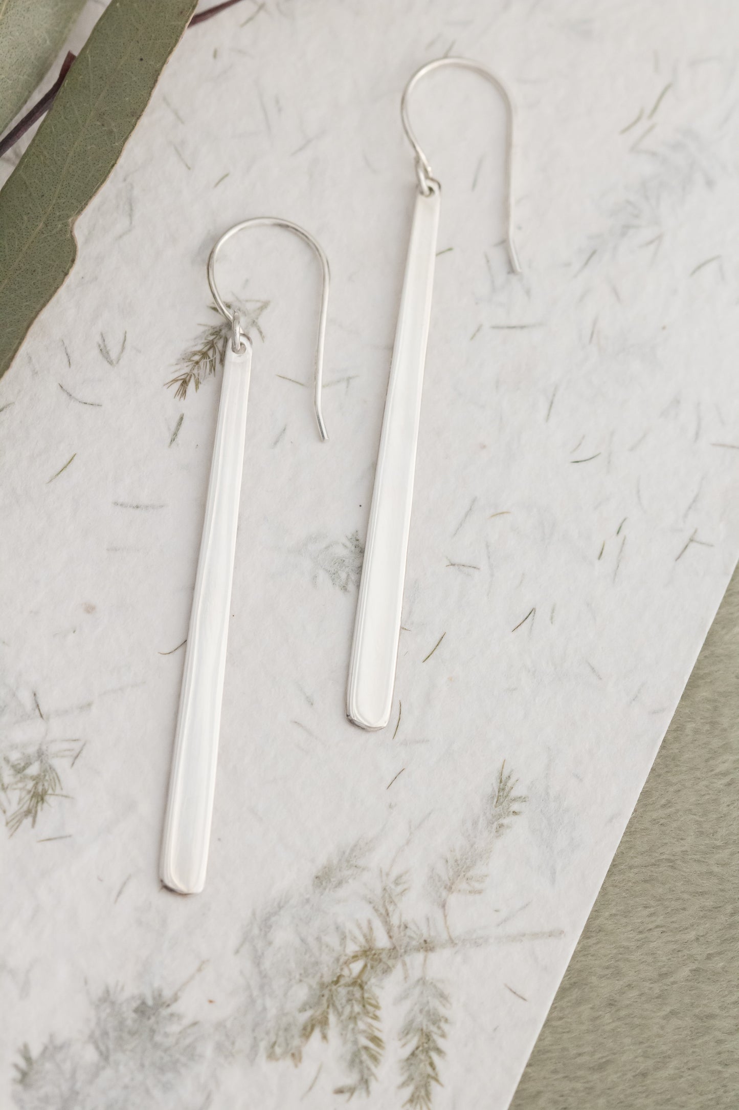 Pair of silver earrings on a textured white surface with dried leaves.