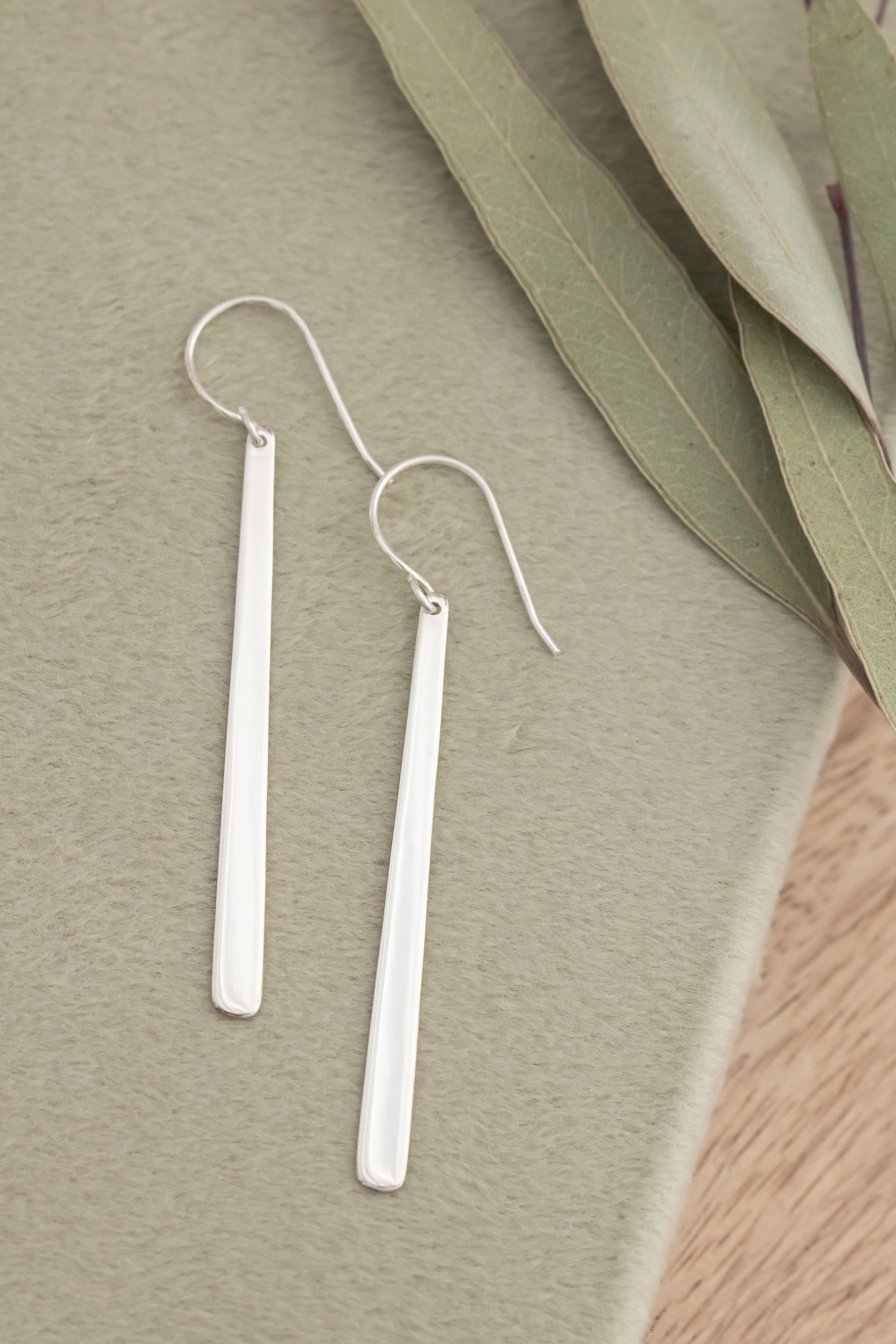 Silver bar earrings on a textured surface with green leaves