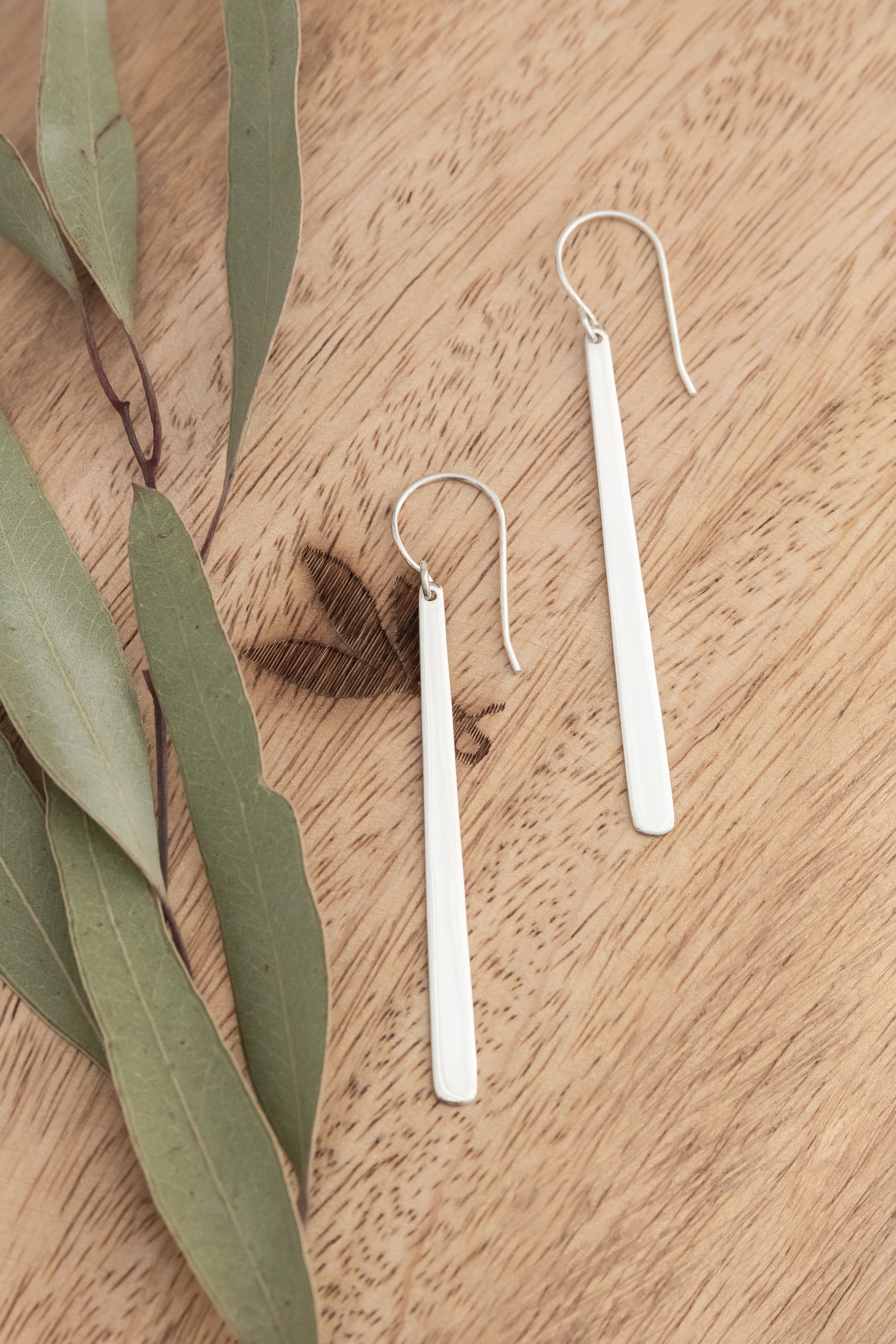 Silver earrings on a wooden surface with eucalyptus leaves