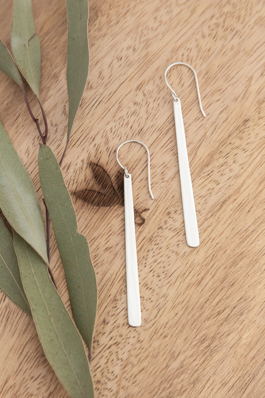 Silver earrings on a wooden surface with eucalyptus leaves