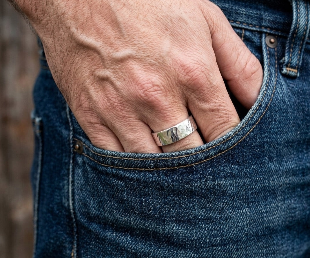 A mans hands with a hammered silver ring in a blue denim pocket