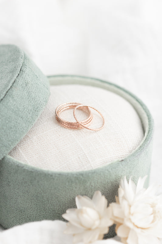 Two rose gold rings in a green jewelry box with white flowers on a light background