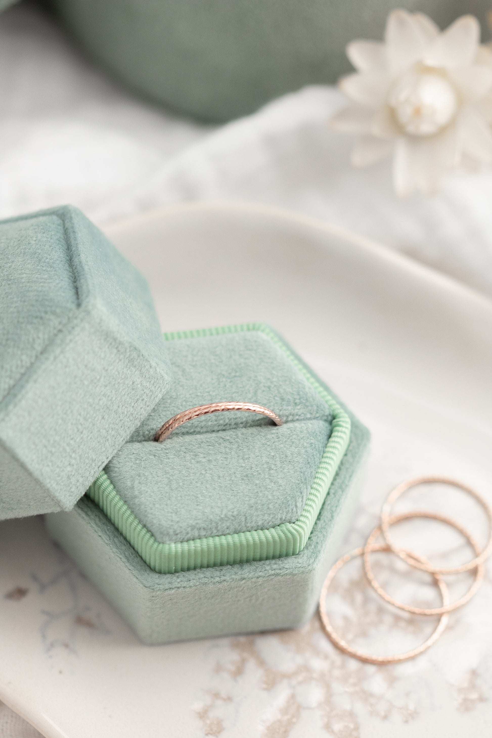 Green hexagonal jewelry box with a ring inside, placed on a light surface.