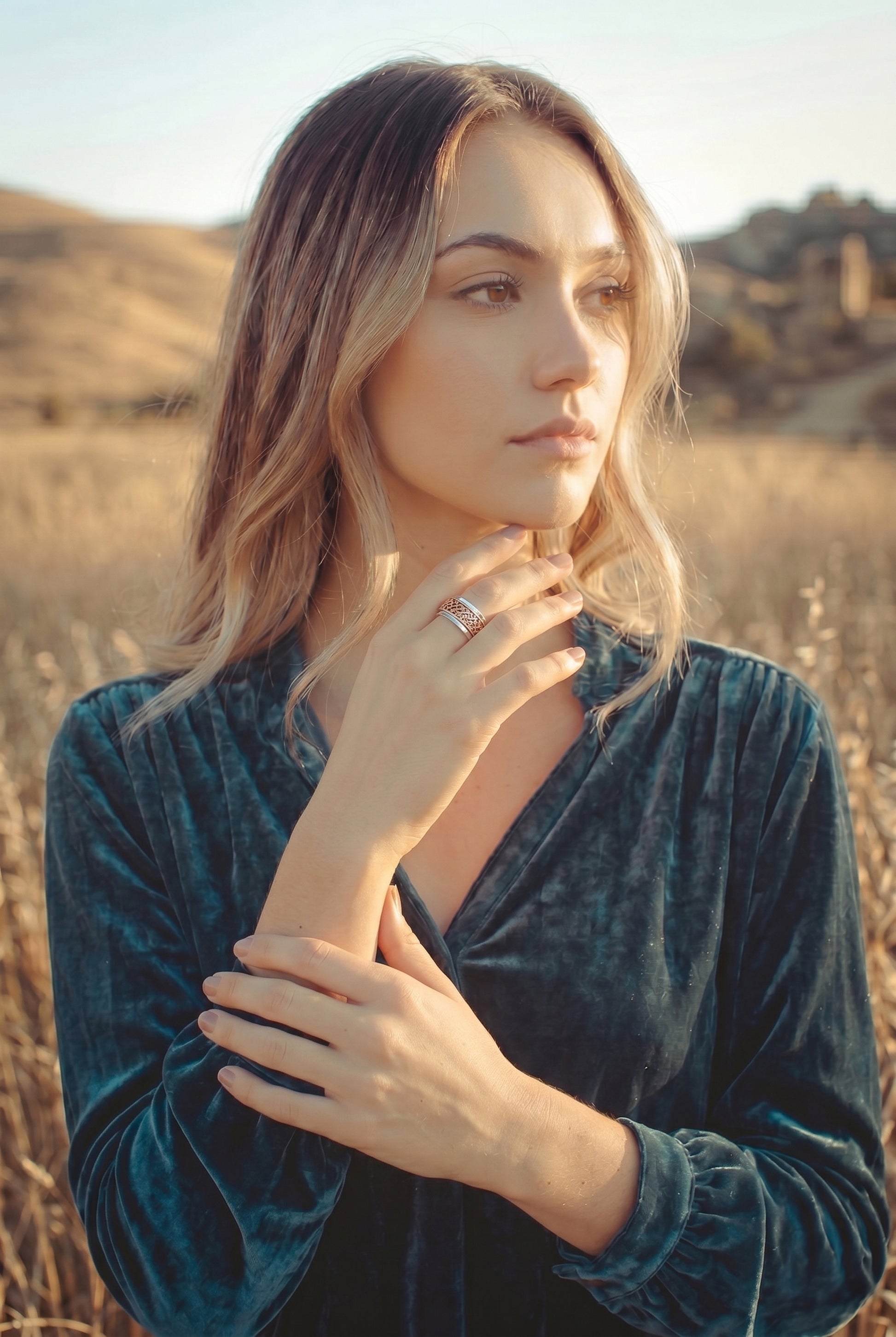 A model wearing a two-tone ring with a sterling silver hammered band and an outer double crown wire copper band the spins freely on a light fabric background with green leaves.