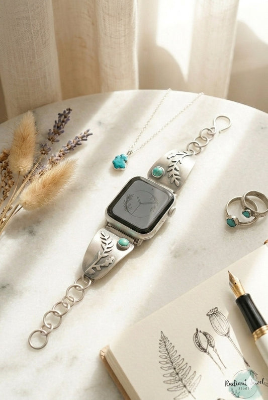Sterling Silver smartwatch with decorative fern design and turquoise stone on a marble surface with flowers and rings.