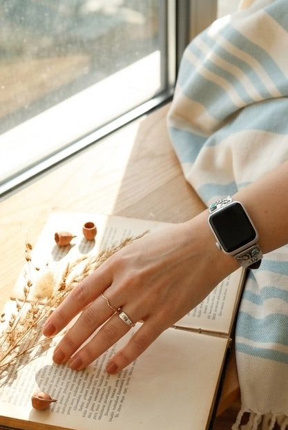 Person wearing a custom sterling silver and turquoise smartwatch band  on an open book with a window in the background