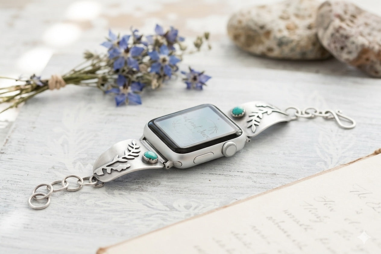Sterling Silver smartwatch with decorative fern design and turquoise stone on a wood surface with flowers and  stones