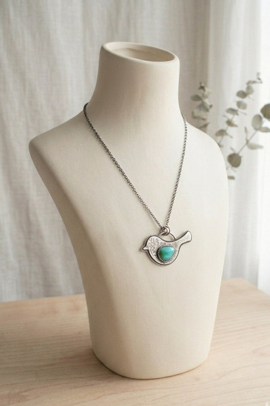 Sterling silver bird shaped pendant necklace with floral design and turquoise wing  on a mannequin bust against a neutral background