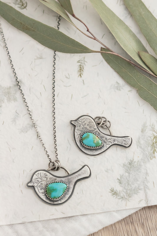 Bird-shaped silver and turquoise pendant necklace on a floral background