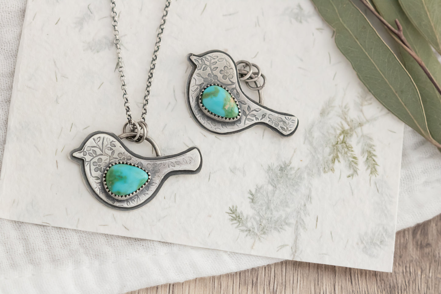 Bird-shaped pendants with turquoise stones on a textured surface