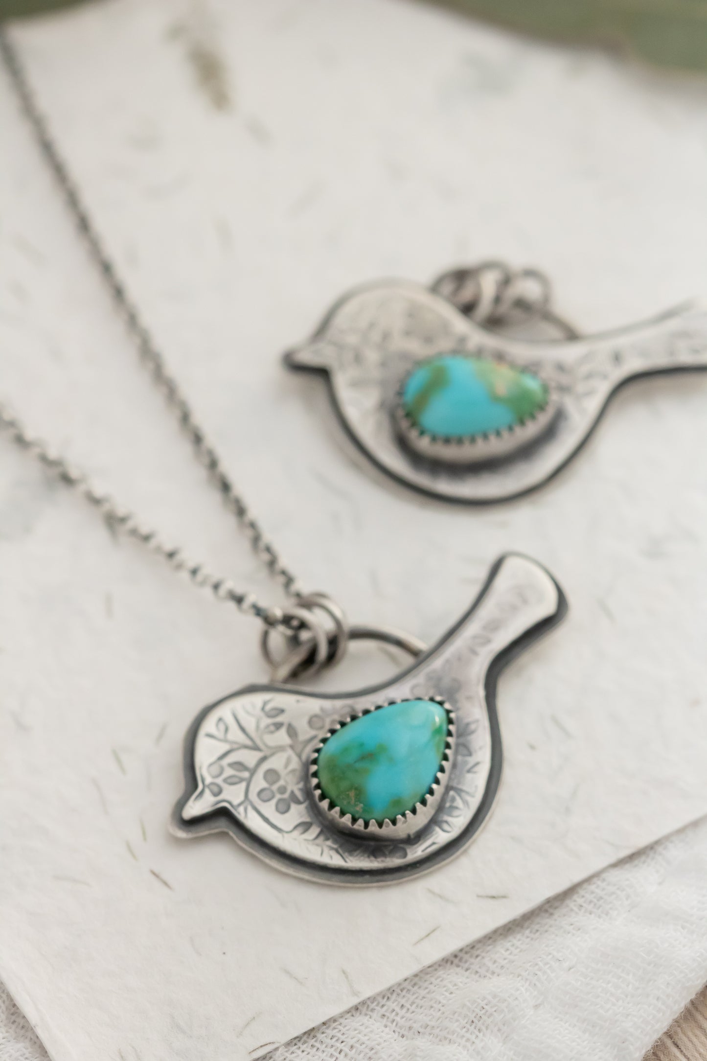 Sterling Silver bird pendants with turquoise stones and floral patterned birds on a textured surface