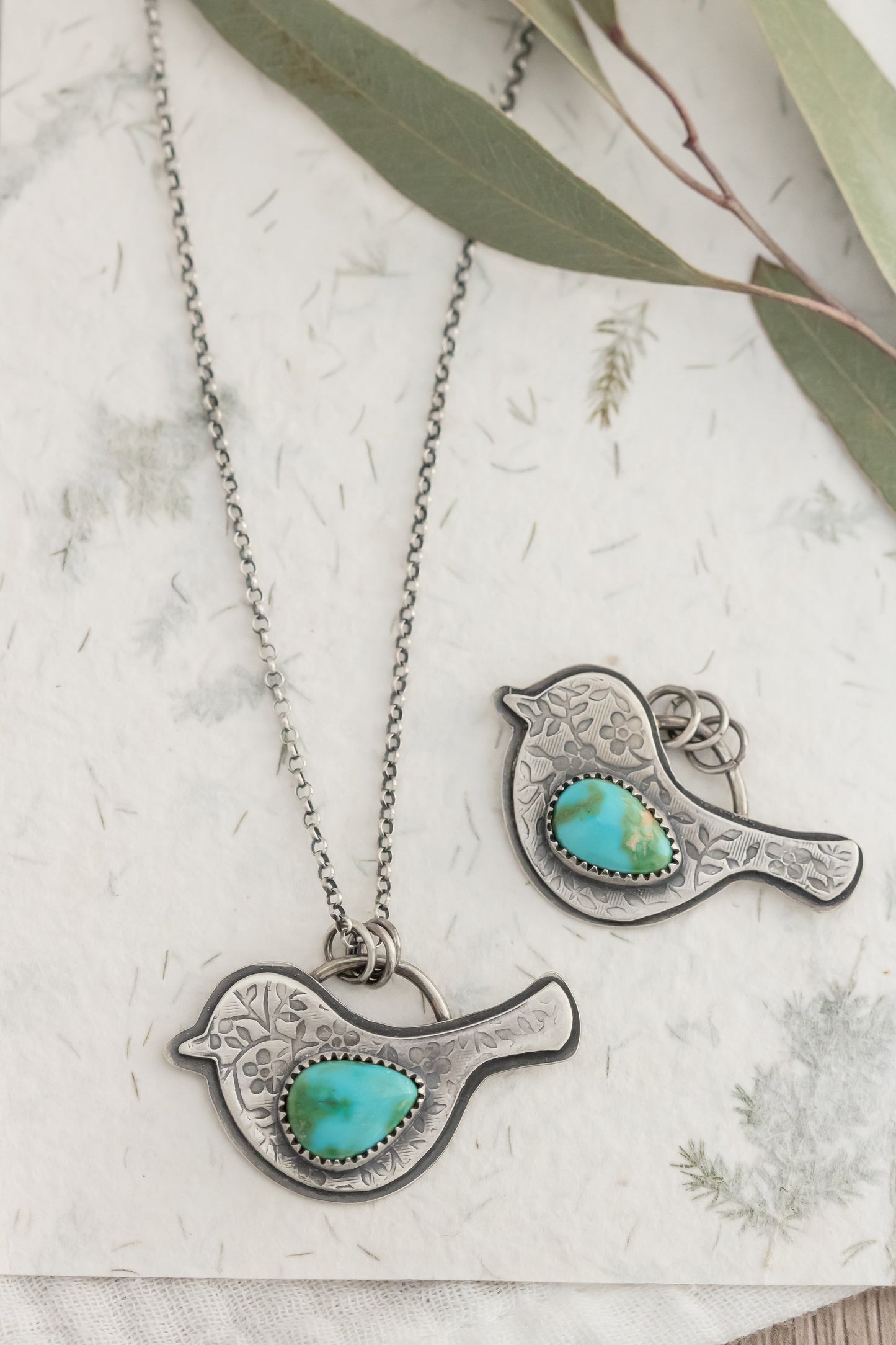 Sterling Silver bird pendants with turquoise stones and floral patterned birds on a textured surface