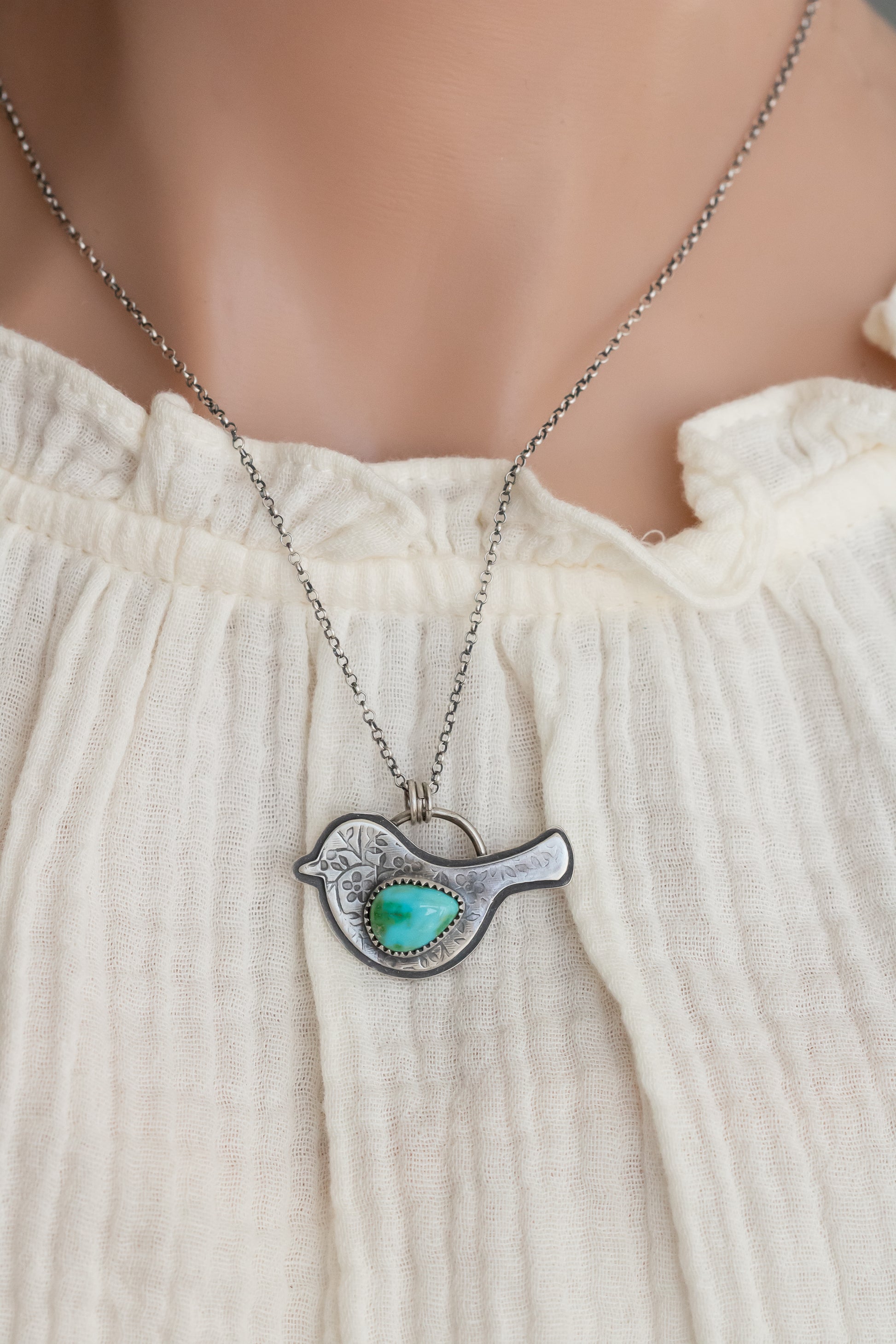 Sterling silver bird necklace with turquoise pendant worn on model in white ruffled shirt, showcasing neckline fit
