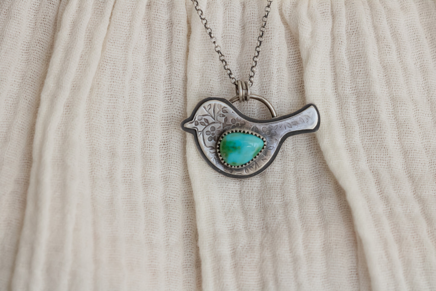Sterling silver bird necklace with turquoise pendant worn on model in white ruffled shirt, showcasing neckline fit
