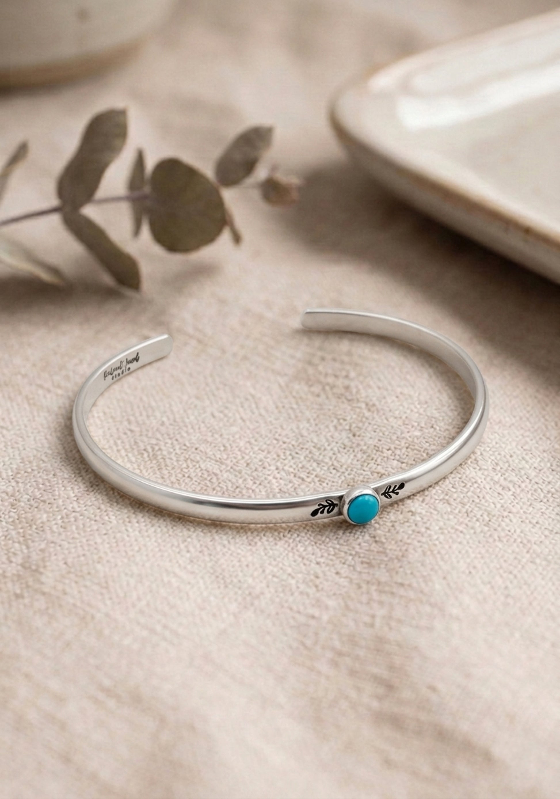 Silver bracelet with a turquoise stone on a beige surface with a plant in the background