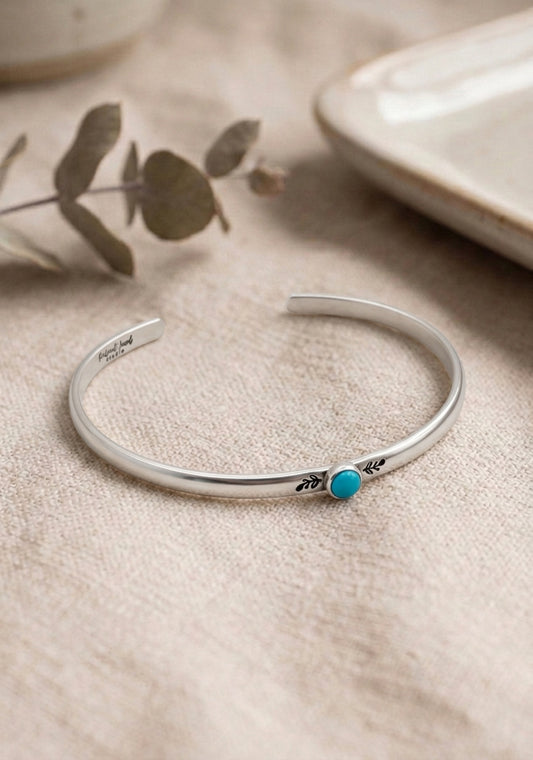 Silver bracelet with a turquoise stone on a beige surface with a plant in the background