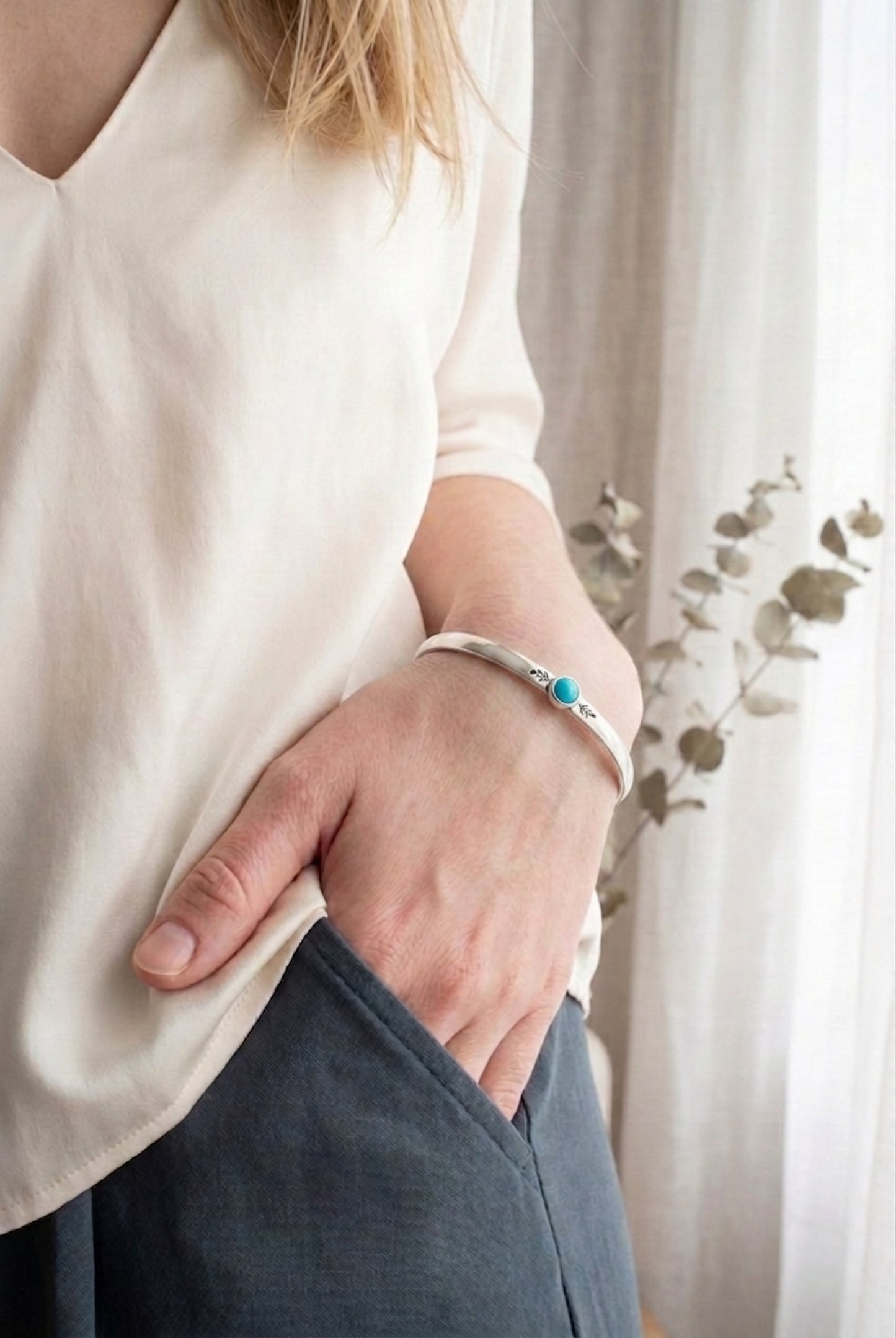 Minimalist sterling silver cuff bracelet with a small, round turquoise gemstone set in a bezel, flanked by delicate leaf engravings, handcrafted for stacking. Dainty jewelry for women.