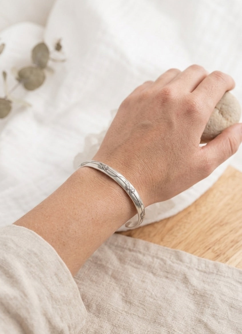 Hand wearing a sterling silver bracelet with a floral vine design  on a light background