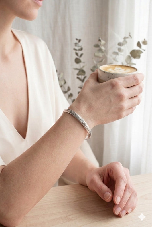 Person wearing a sterling silver cuff bracelet with floral vine design, holding a cup of coffee with a blurred background