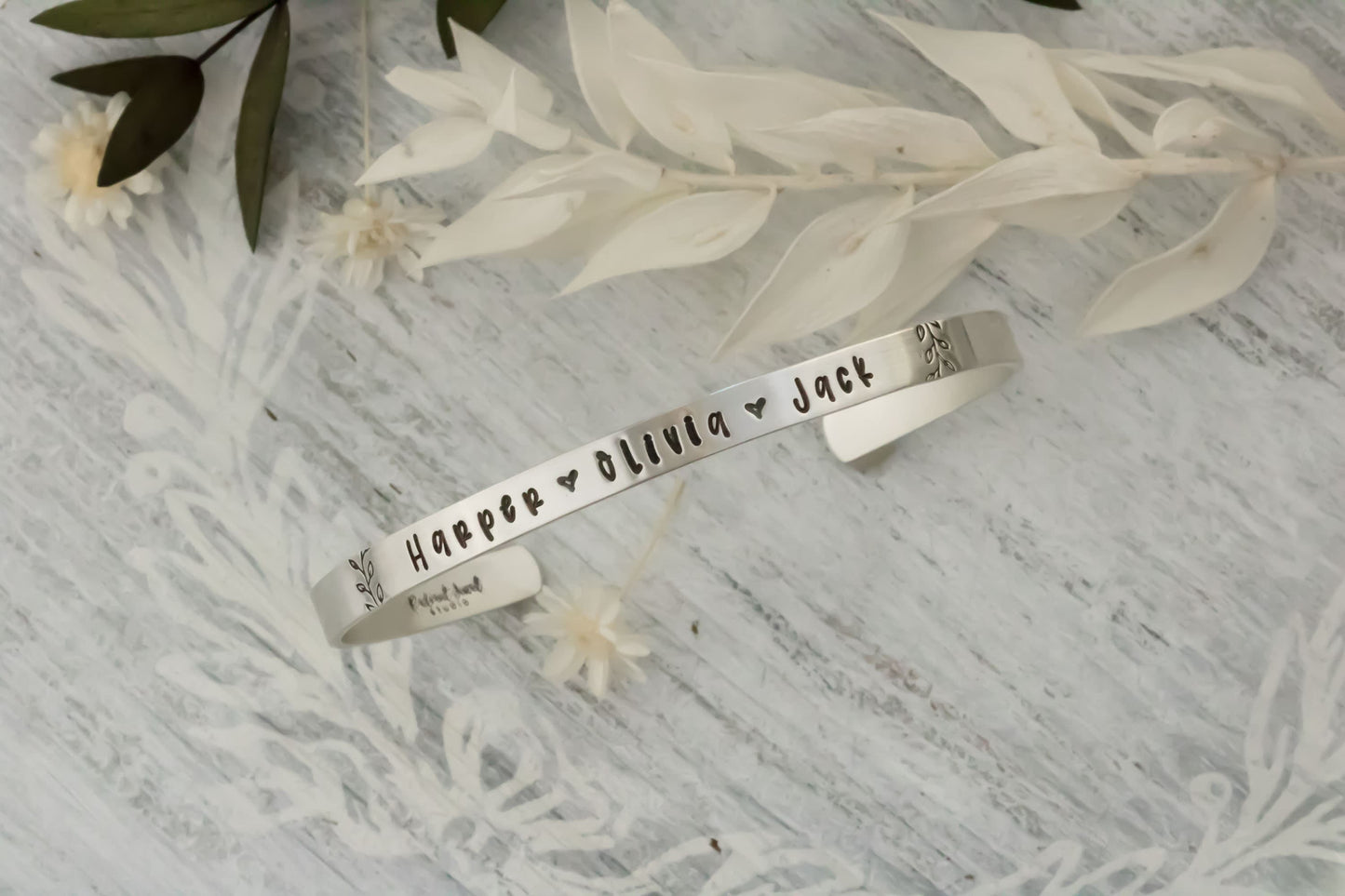 Sterling silver cuff bracelet stamped with kids names in a delicate handwritten font with a stamped for detail on both sides.