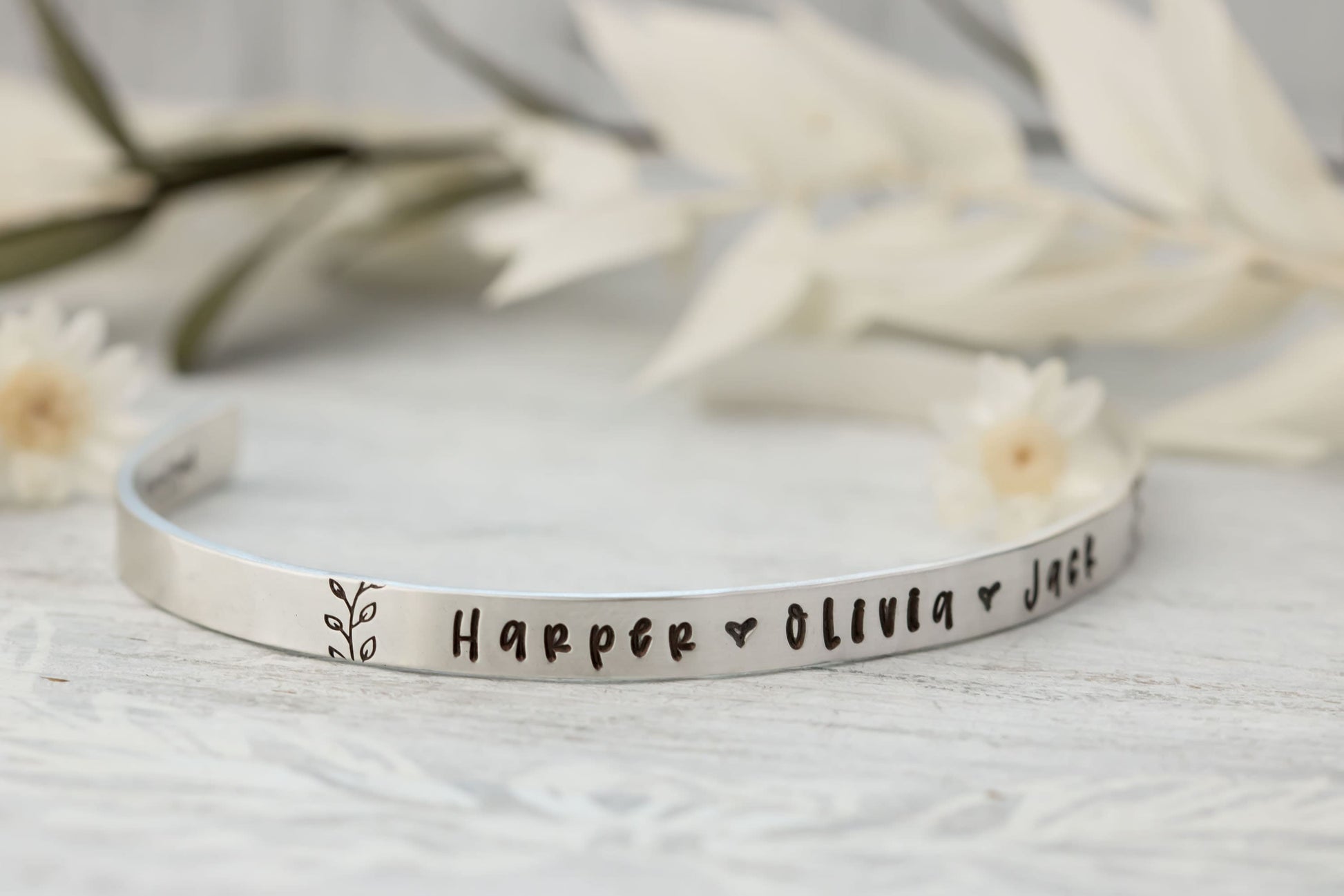 Sterling silver cuff bracelet stamped with kids names in a delicate handwritten font with a stamped for detail on both sides.