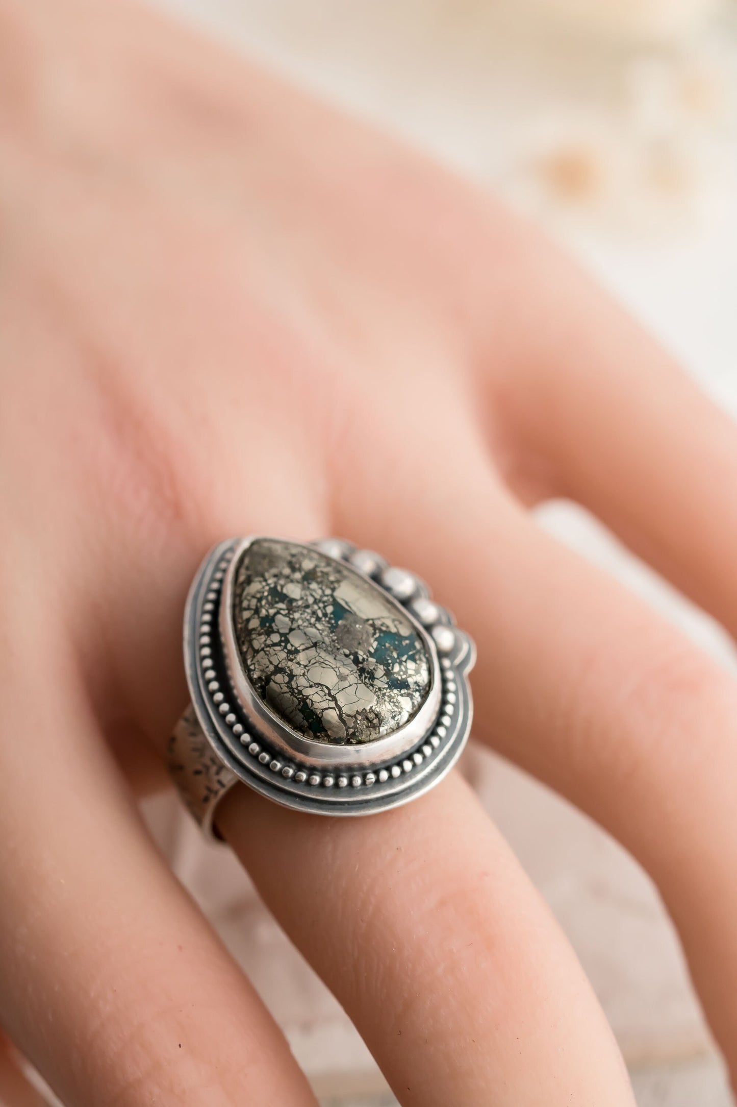 Sterling silver wide band ring will floral design, a morinci 2 turquoise pear shaped cabochon with pyrite inclusions and beaded accent bezel